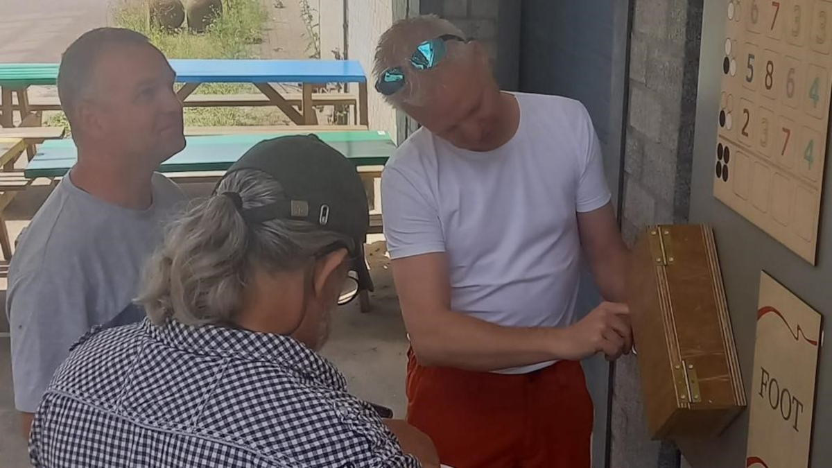 Drie personen proberen een kistje met cijferslot te openen.