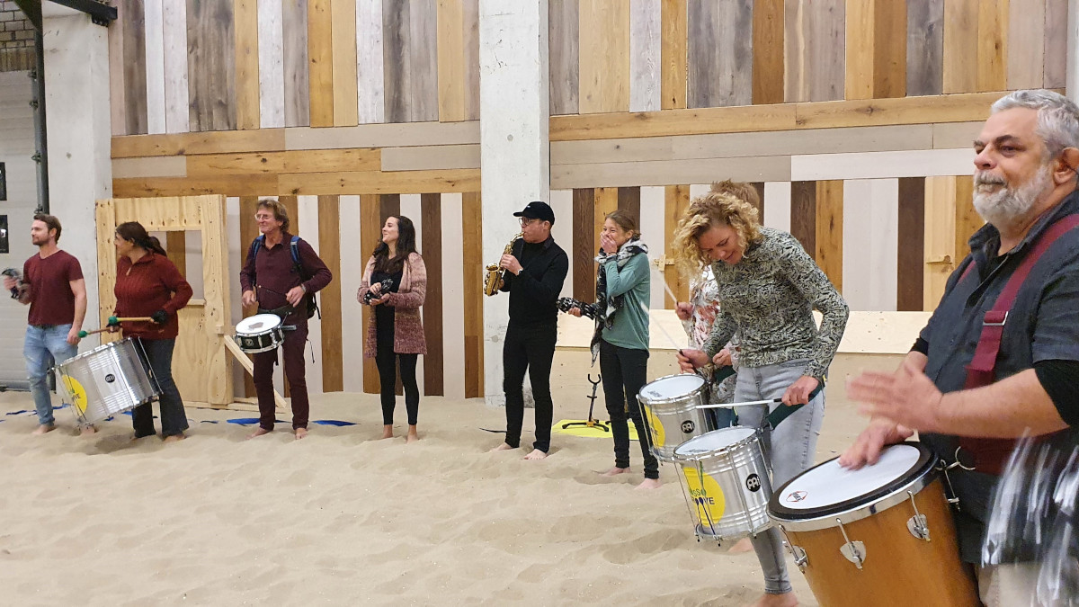 Een groep mensen die deelnemen aan de percussie workshop op het zand.