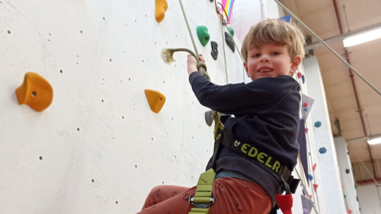 Een jongen hangt aan het touw en wordt naar beneden begeleid tijdens het Kinderfeestje Klimmen.