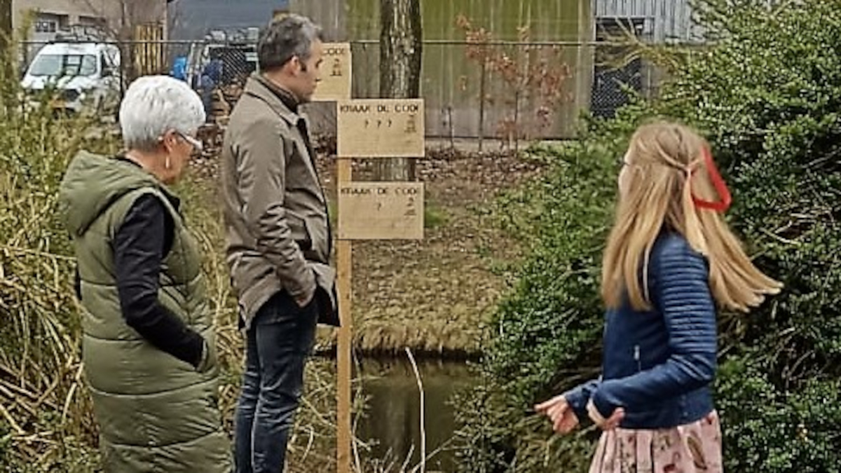 Drie personen staan bij de puzzels aan het water en proberen deze op te lossen.