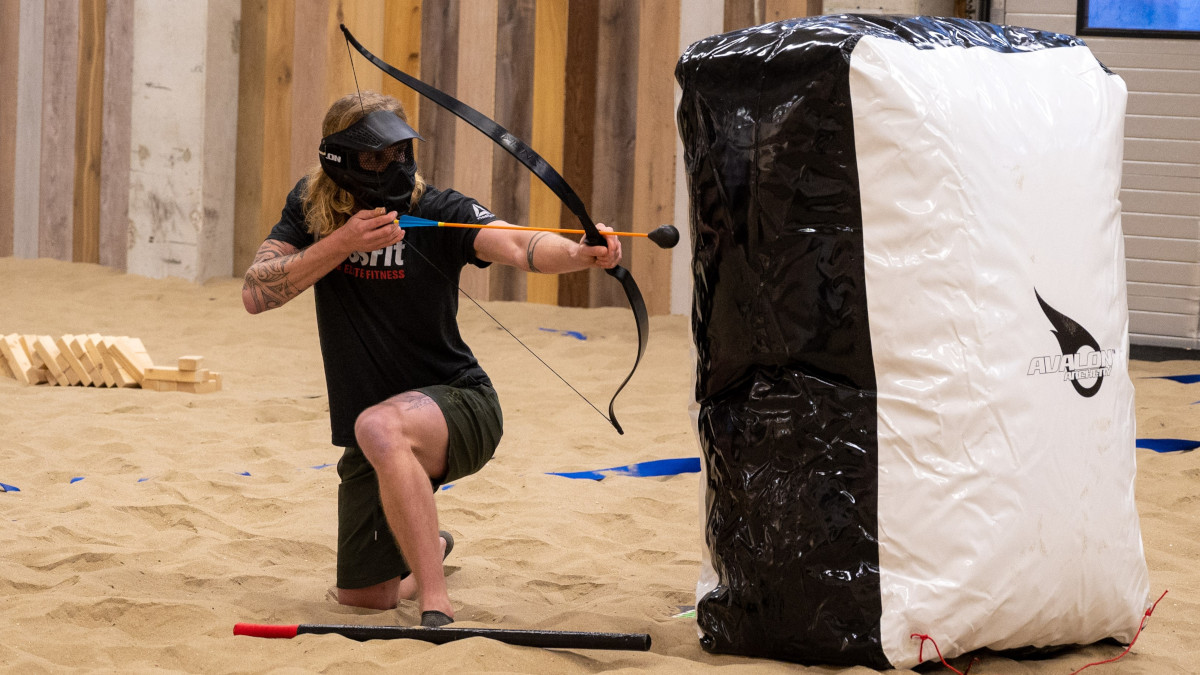 Een persoon schuilt achter een obstakel tijdens Archery Tag en richt een pijl op de tegenpartij.