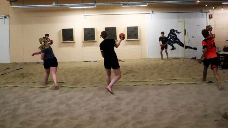 Drie personen gooien tegelijk een bal naar de tegenpartij tijdens dodgeball op het indoor strand.