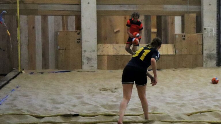 Een dodgeball wordt gegooid naar een jongen van het andere team die deze probeert te ontwijken terwijl hij in de lucht hangt.