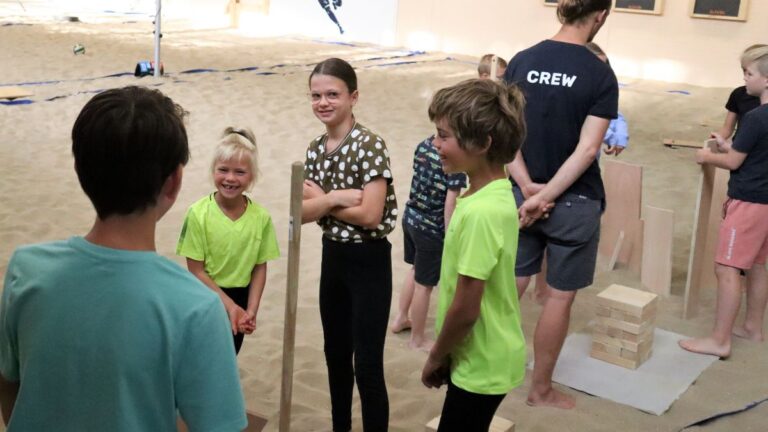 Een aantal kinderen staan op het zand en hebben plezier.