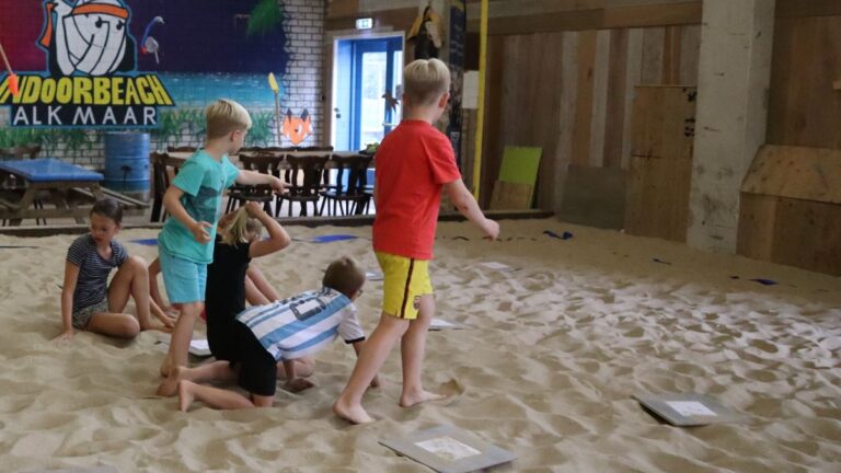 De kinderen spelen levend ganzenbord op het zand.