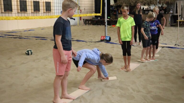 Een aantal kinderen speelt een spel waarbij ze over planken moeten lopen, maar de grond niet mogen aanraken.