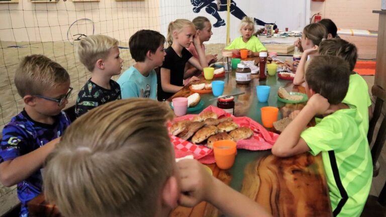 De kinderen van het zomerkamp zitten aan tafel voor de lunch.
