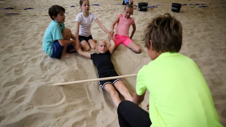 Een meisje wordt geholpen en onder de balk over het zand door getrokken.