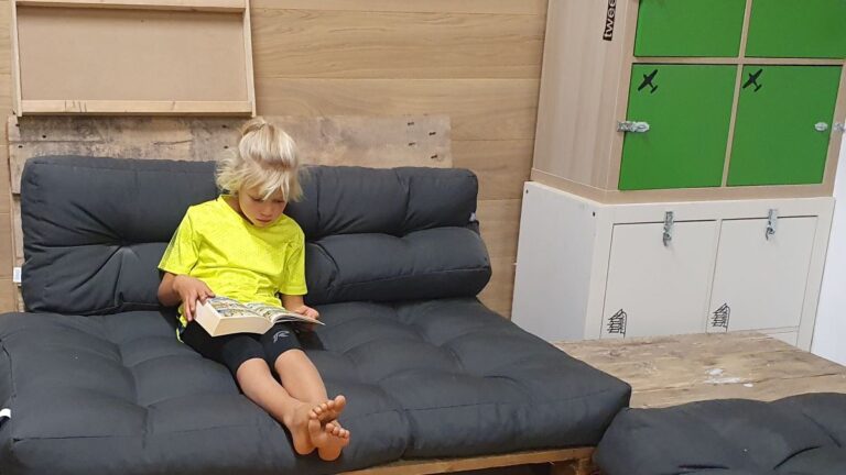 Een meisje op de bank dat tijdens het zomerkamp lekker rustig een stripboek leest.