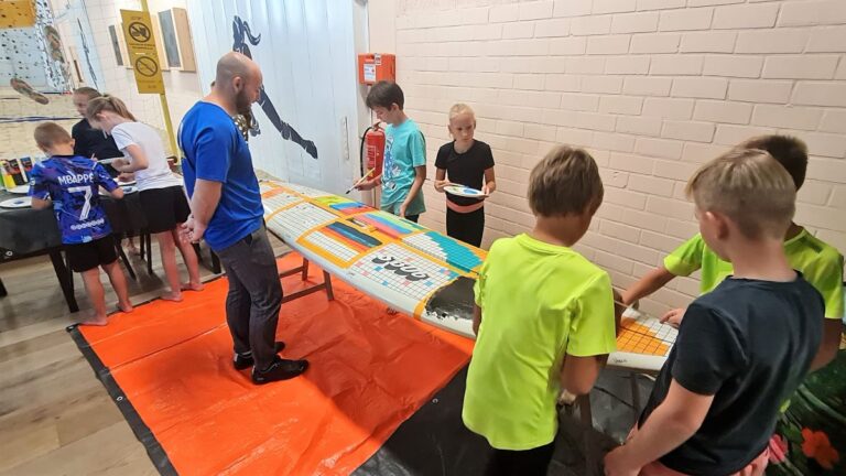 Mike komt even kijken hoe het gaat bij de kids met het beschilderen van de surfplank.