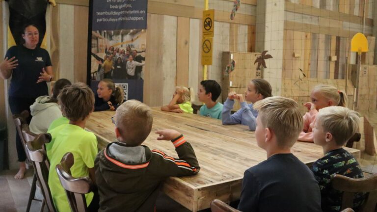 De instructeur legt de regels uit, de kids zitten aan tafel.