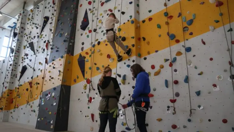 Onder begeleiding van een instructeur is een moeder haar zoon aan het zekeren die op de klimwand aan het klimmen is.