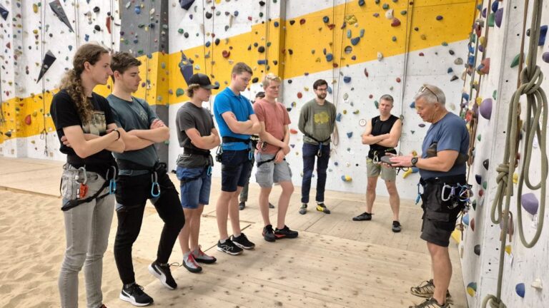 Een groep deelnemers aan de Indoor Toprope cursus bij Indoor Beach Alkmaar krijgt uitleg van de instructeur bij de klimwand.
