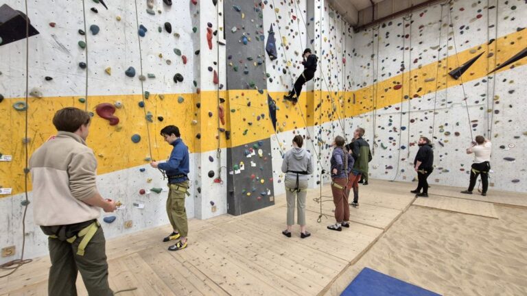 Meerdere deelnemers aan de Indoor Toprope Cursus staan bij de klimwand.