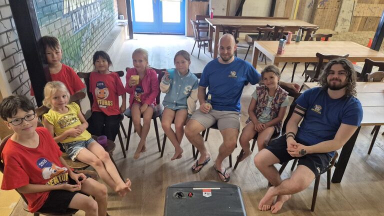 Aventuras Zomerkamp bij Indoor Beach Alkmaar. De groep kinderen en begeleiders warmen zich op bij de kachel.