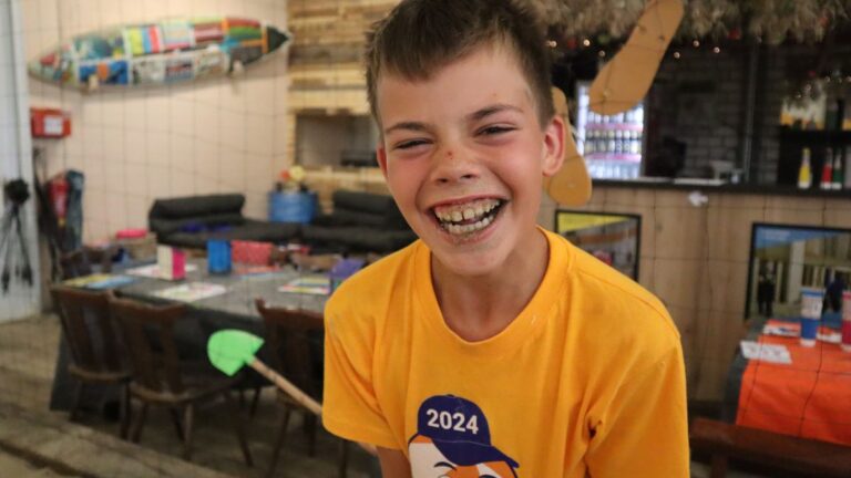 Aventuras Zomerkamp bij Indoor Beach Alkmaar. Een jongen lacht, terwijl zijn mond vol met zand zit.
