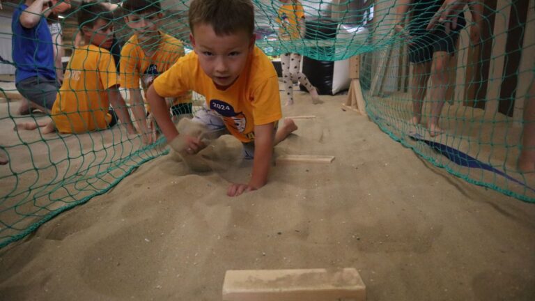 Aventuras Zomerkamp bij Indoor Beach Alkmaar. Een jongen kruipt onder de kruipnetten door.