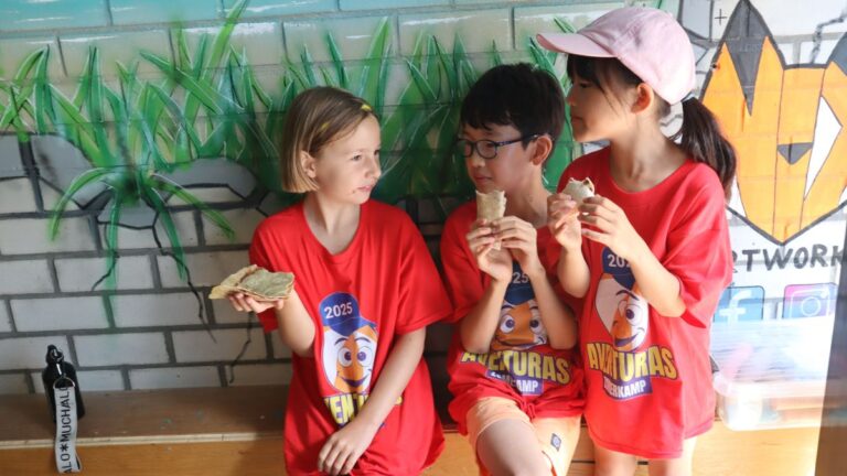 Aventuras Zomerkamp bij Indoor Beach Alkmaar. Drie kinderen eten samen.