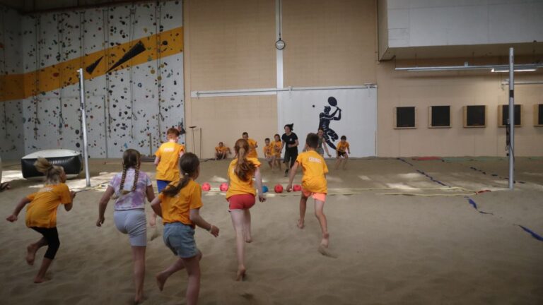 Aventuras Zomerkamp bij Indoor Beach Alkmaar. Een groep kinderen rent naar de bal om trefbal te spelen.