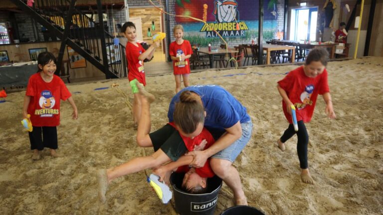 Aventuras Zomerkamp bij Indoor Beach Alkmaar. Een jongen wordt met zijn hoofd in een emmer water gestopt tijdens het waterpistolen gevecht.